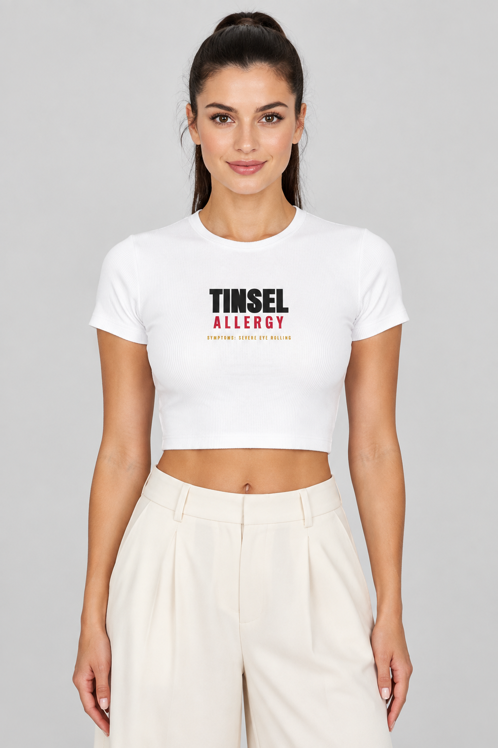Woman with a dark high ponytail in the white Tinsel Allergy crop tee, studio backdrop